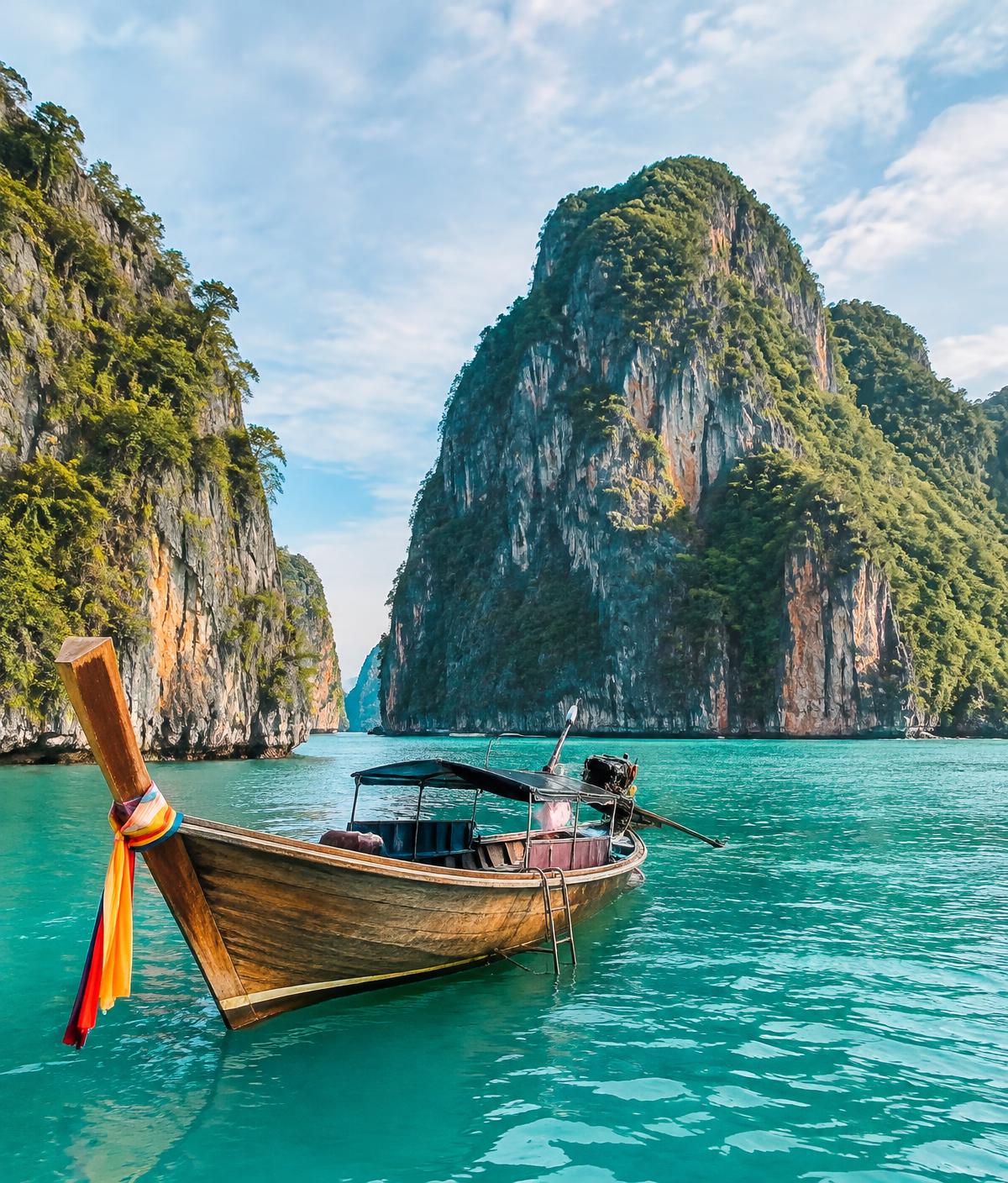 A traditional longtail boat on turquoise water between limestone cliffs in Thailand